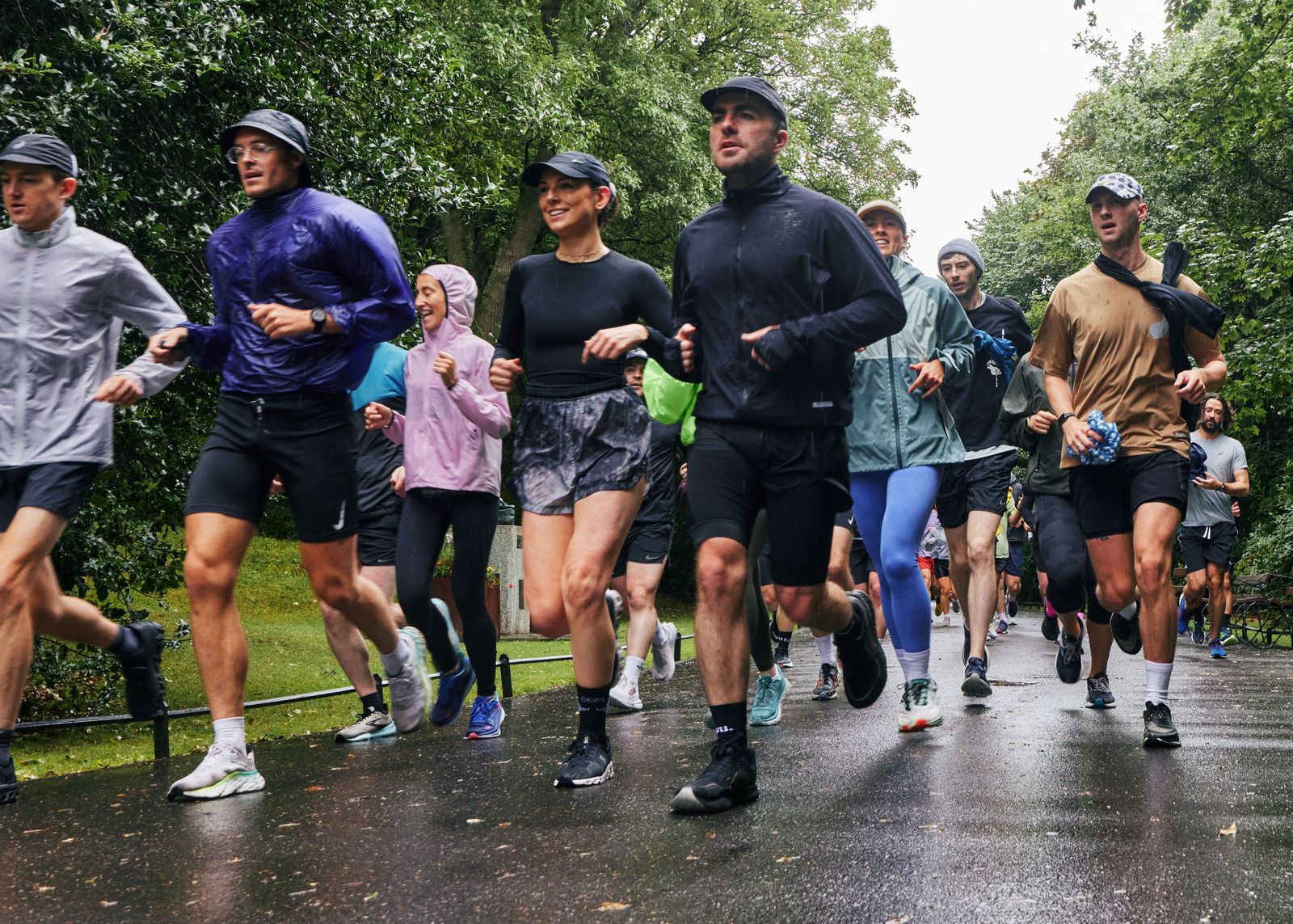 A pack of runners in rain jackets running on a wet path, smiling.